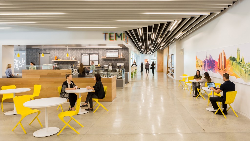 A group of people sitting at tables in a room with a large screen.