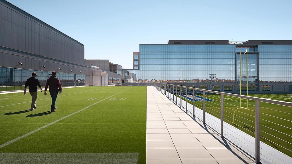 A couple of men walking on a grass field in front of a building.