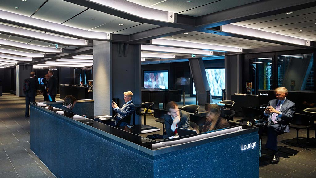 A group of people sitting at a table in a room with large screens.