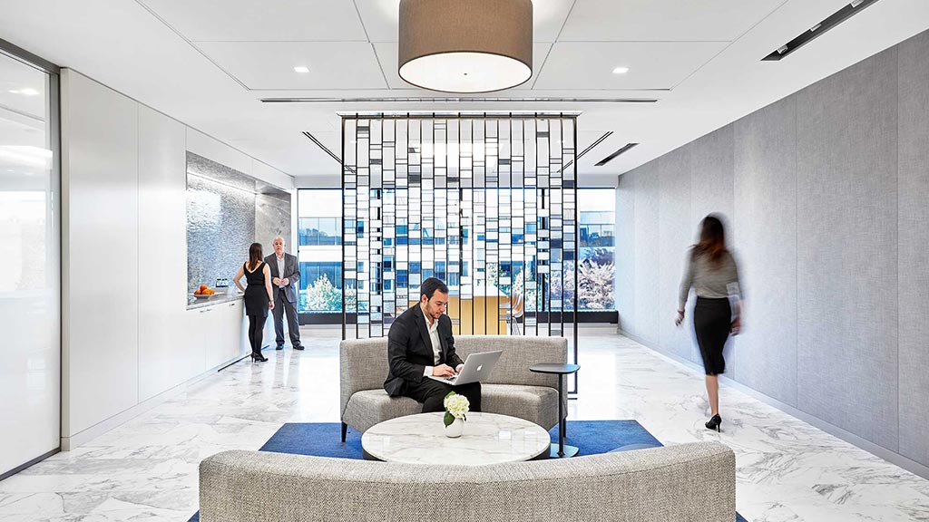 A person sitting on a couch in a room with people walking around.