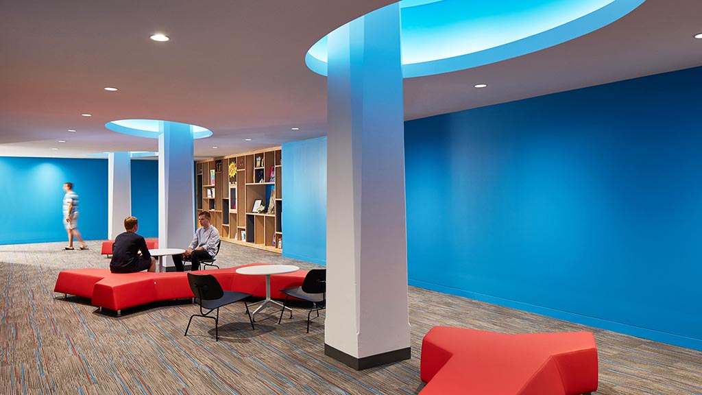 A man and a woman sitting in a room with a red couch and a table.