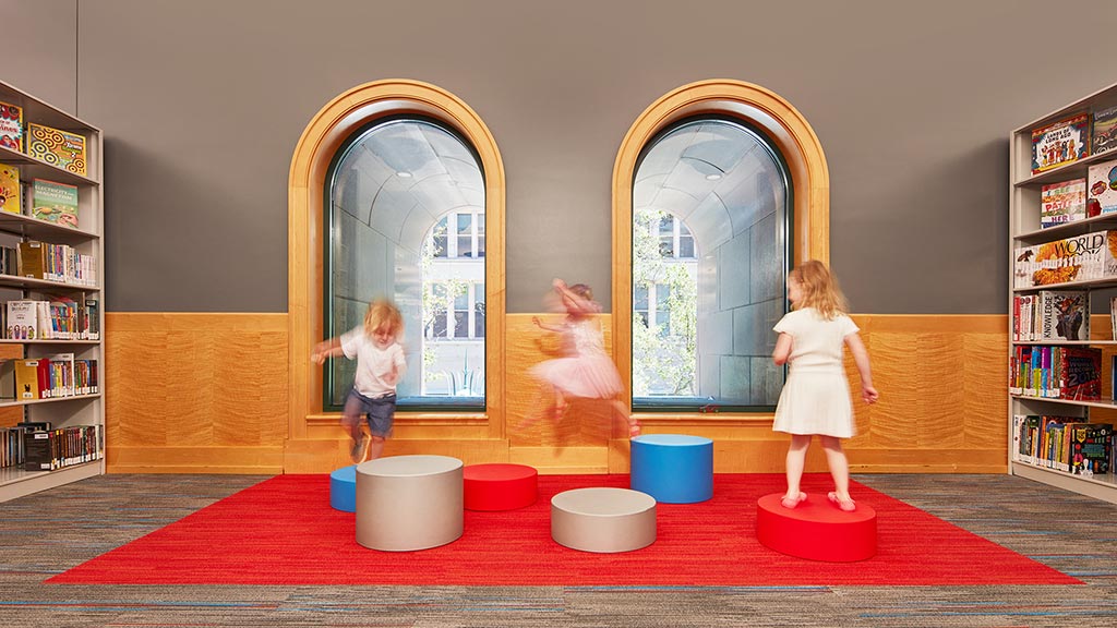 A group of children playing on a red carpet in a library.