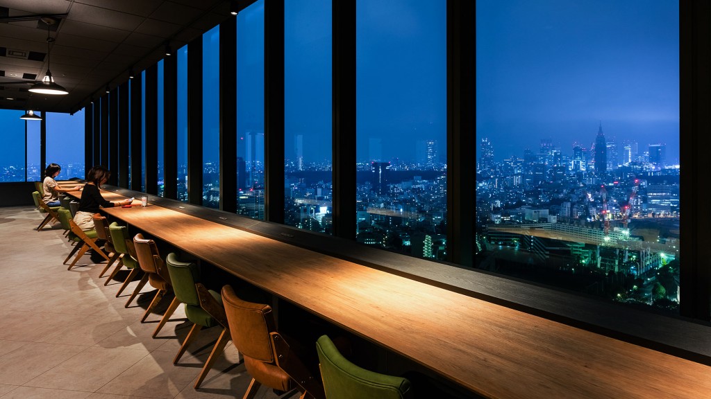 A couple of people sitting at a table in a restaurant overlooking a city.