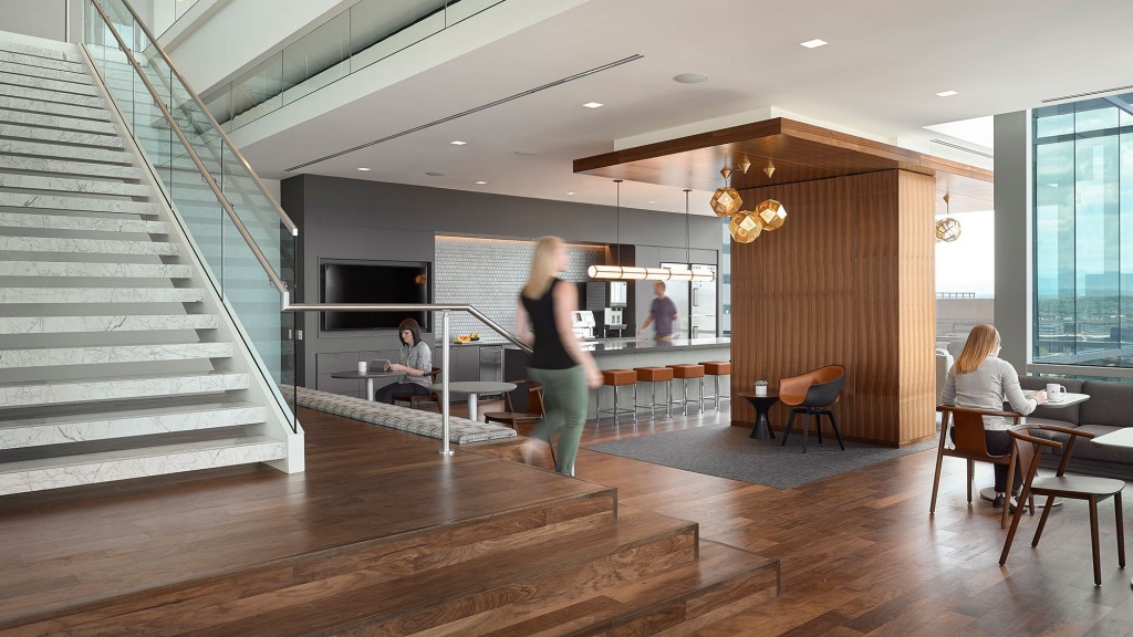 A person standing in a room with people sitting at tables and chairs.