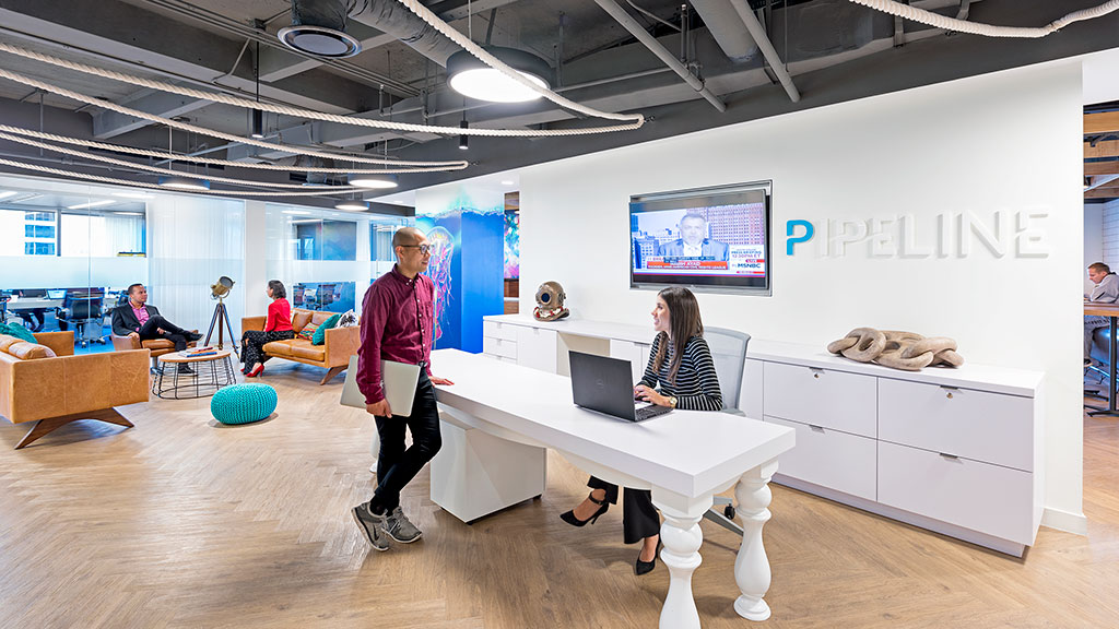 A man and a woman in a room with a laptop and a projector screen.