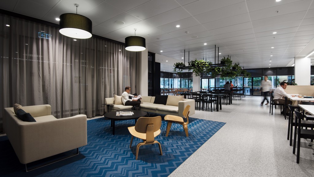 A room with a blue carpet and chairs and a person sitting on a couch.