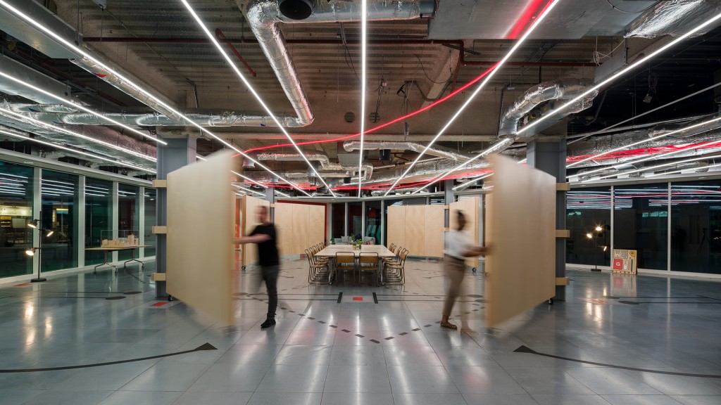 A couple of people walking in a large room with a table and chairs.