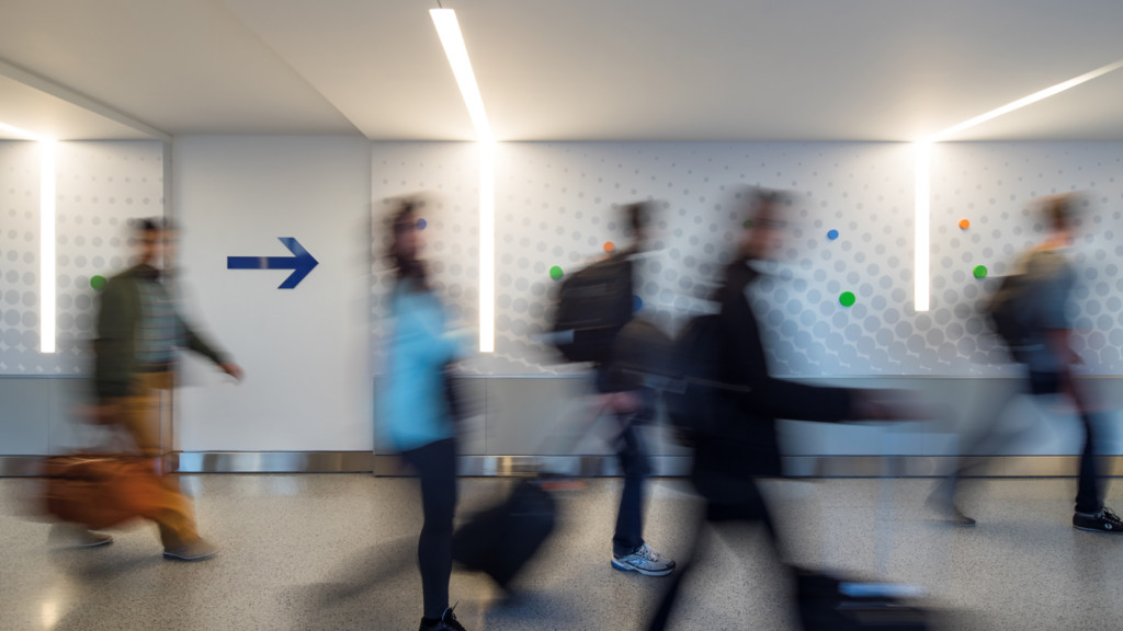 A group of people walking in a room with a white wall and a light.