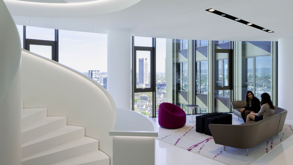 A couple of women sitting on a couch in a room with windows.