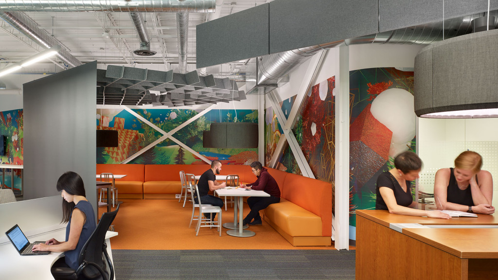 A group of people sitting at a table in a room with art on the wall.