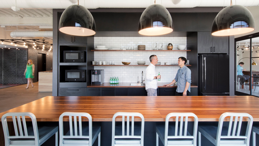 A couple of people standing in a kitchen.