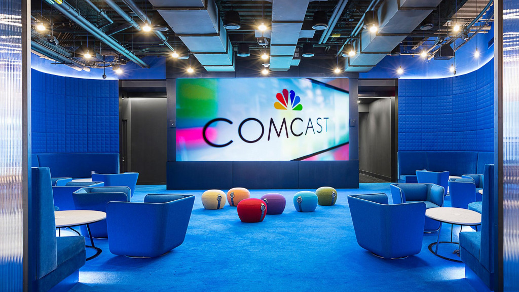 A room with blue chairs and a screen with a logo on it.