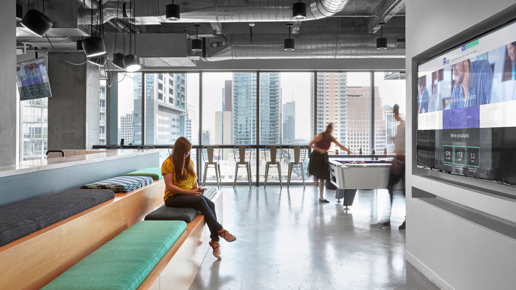 A person sitting on a bench in a large room with a large screen.