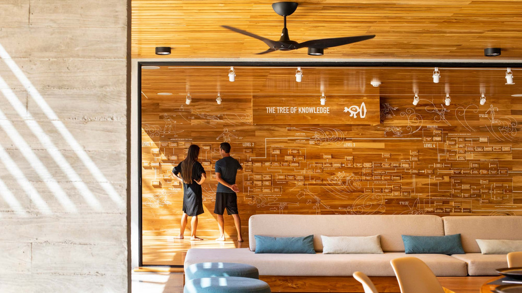 A man and woman standing in a room with a wood wall and a couch.