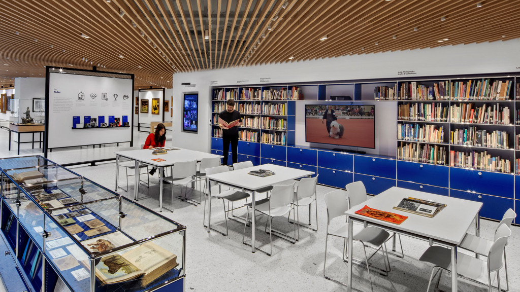 A room with tables and chairs and a large screen with a few people.