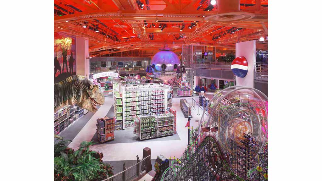 A large indoor space with a dinosaur and a large building with a large statue.