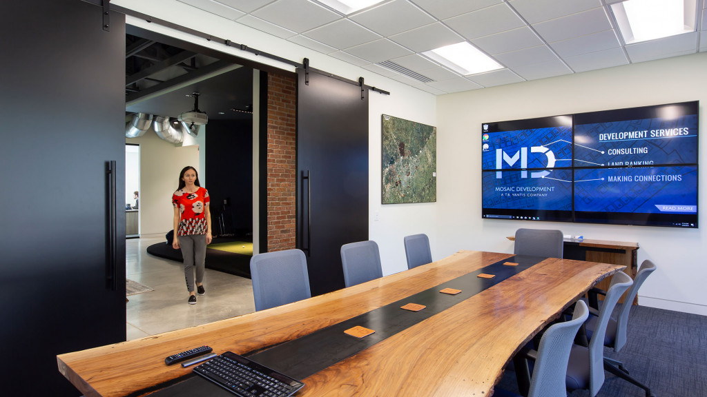 A person standing in a room with a large screen and chairs.