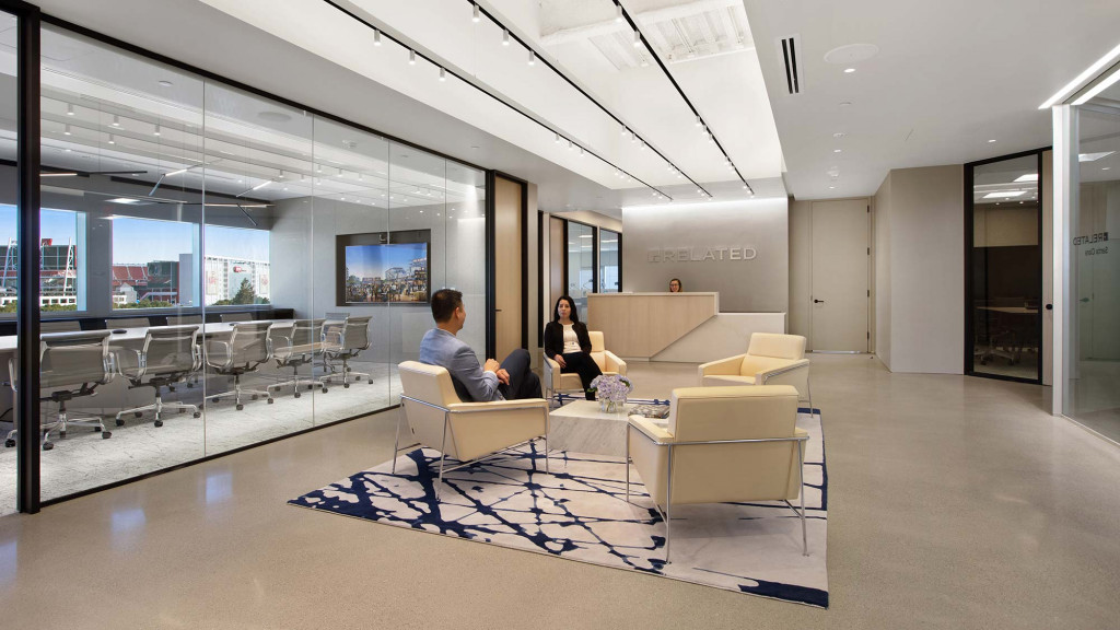 A man and woman sitting in a room with a large screen and chairs.
