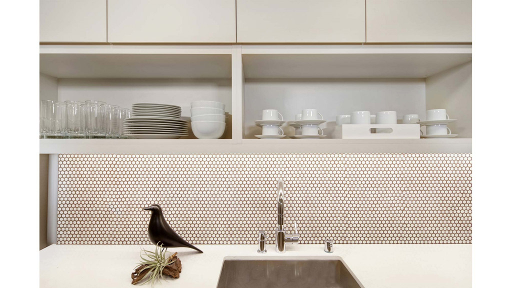 A kitchen with a sink and a shelf with glasses and plates.