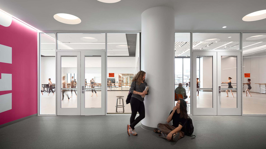 A person standing in a room with a couple of people sitting on the floor.