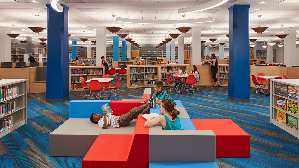A group of people sitting on a red and white table in a library.