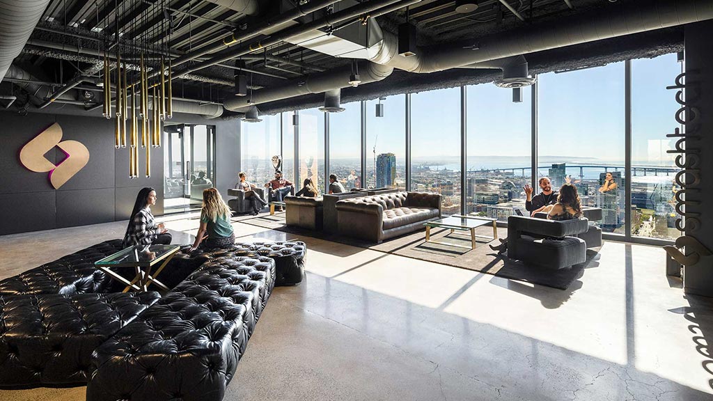 A group of people sitting in a room with large windows.