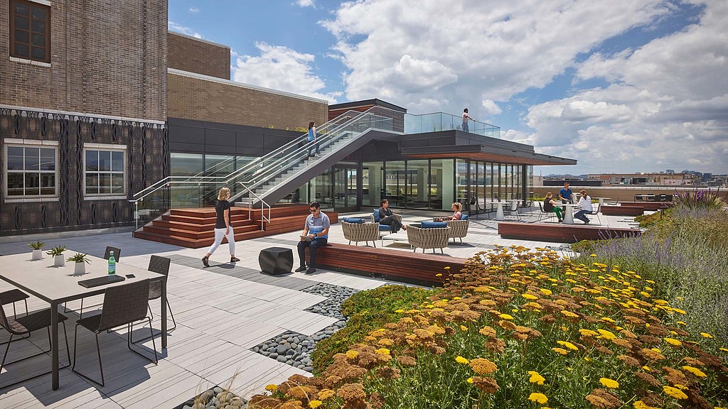 A building with a glass front and a pool with people sitting at tables.
