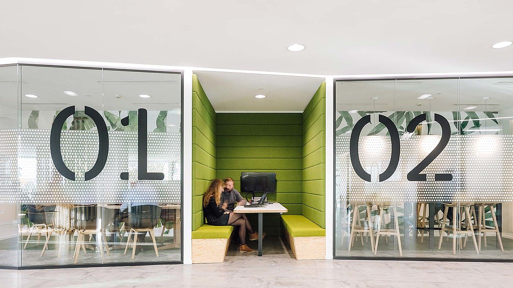 A man and woman sitting at a table in a room with a green wall and a glass door.