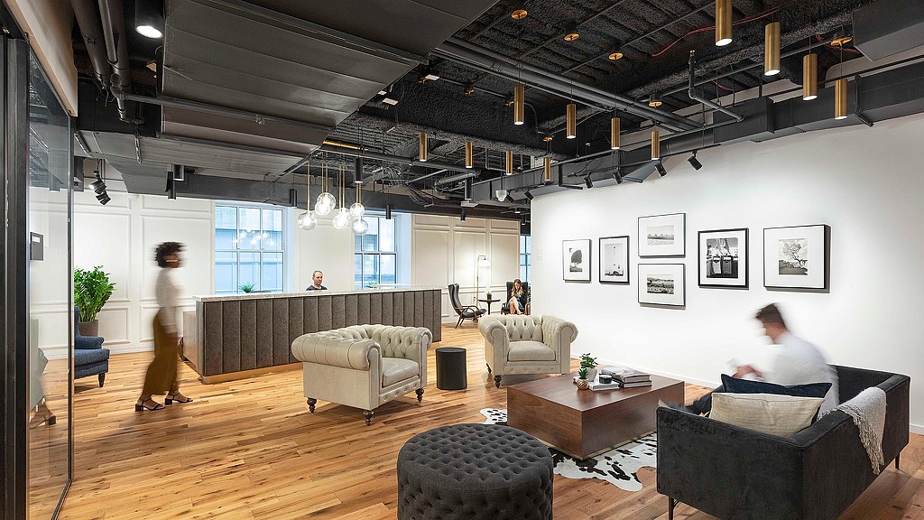 A person sitting on a couch in a room with a wood floor and a large glass ceiling with.