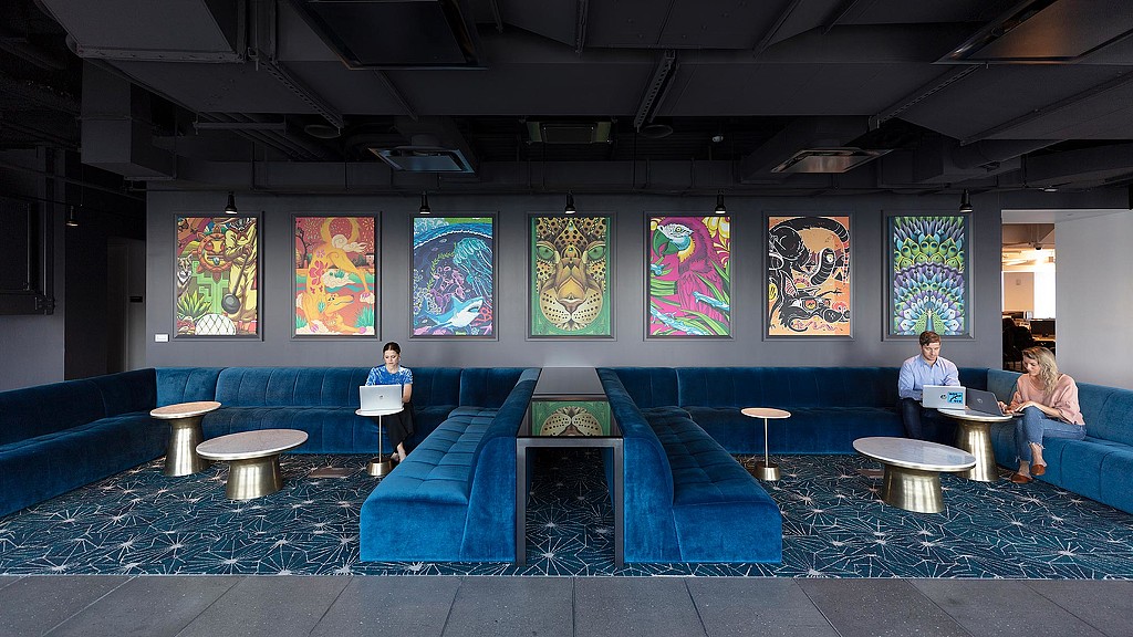 A group of people sitting on a couch in a room with art on the walls.