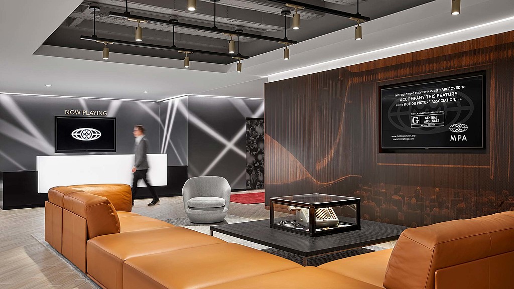 A person walking in a room with a large screen and chairs.