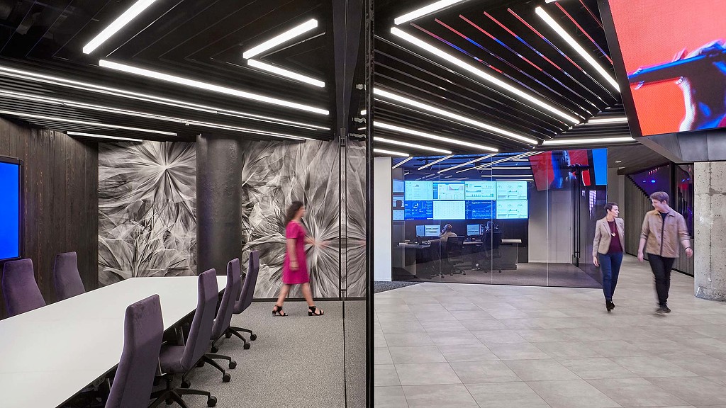 A group of people walking in a room with a large screen.