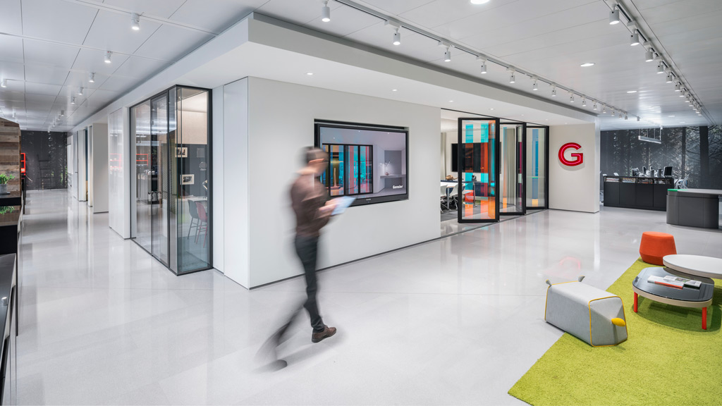 A person walking through an empty architectural office with conference rooms, reception, and workstations in the background.