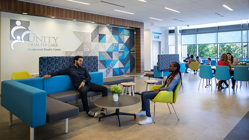 A man and a woman sitting on a couch in a room with blue chairs and a table.