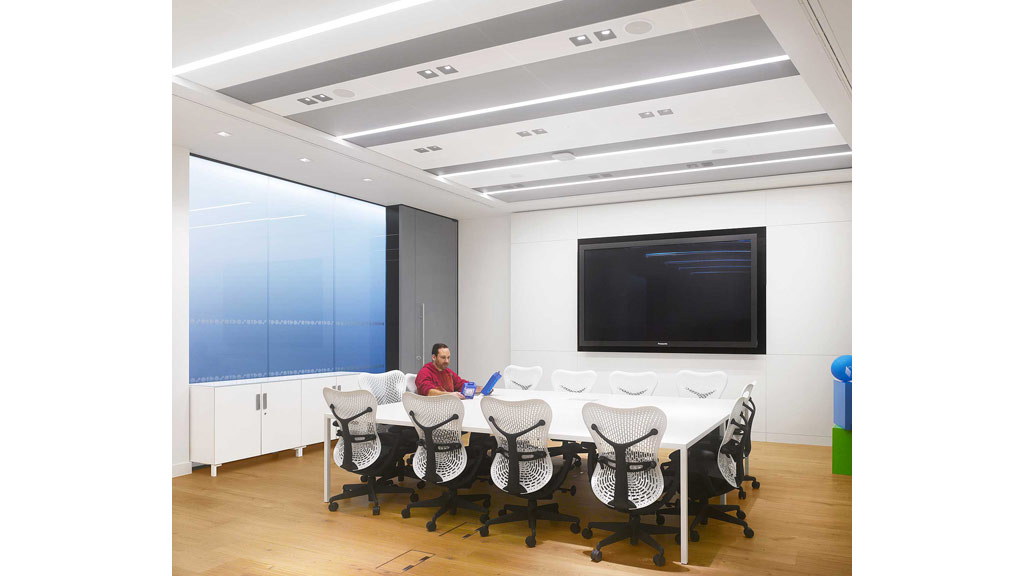 A person sitting at a table in a room with a large screen.