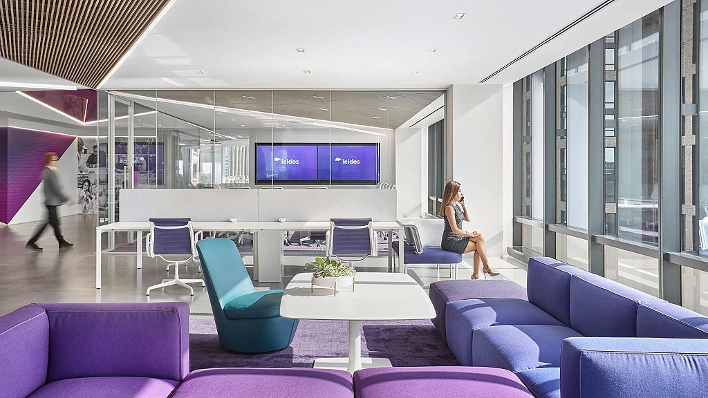 A person sitting on a couch in a room with purple chairs.