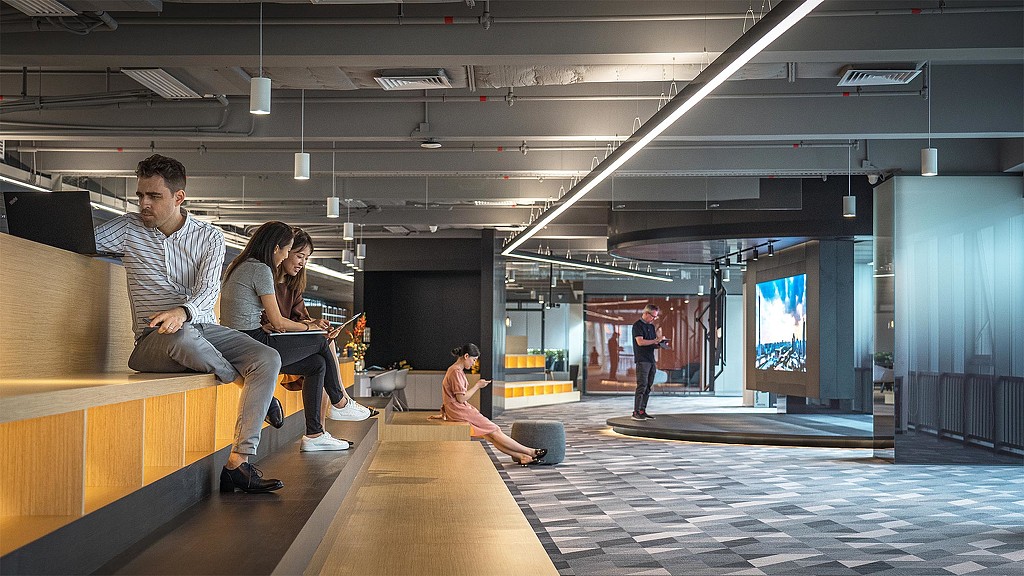A group of people sitting on a bench in a large room.