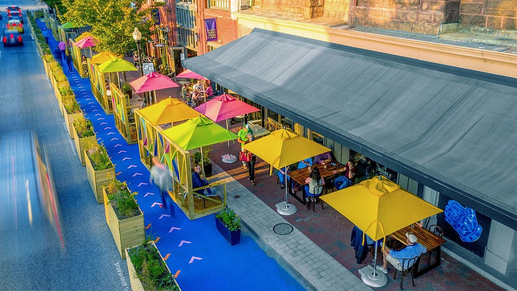 A group of tables and chairs with umbrellas on a street.