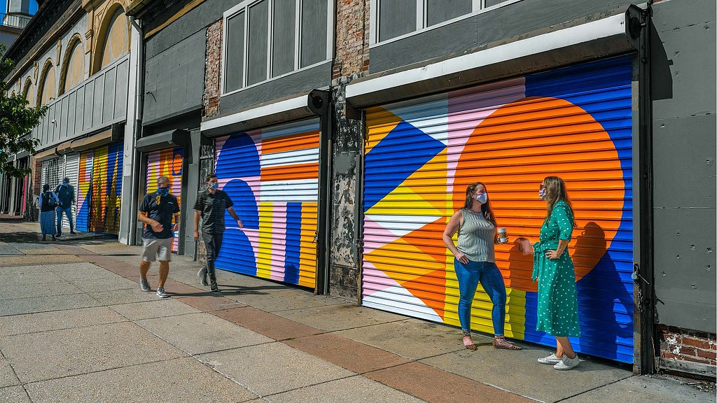 A group of people walking on a sidewalk next to a building with a mural on it.
