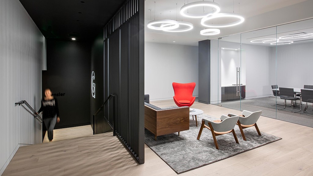 A person walking in a room with chairs and a rug.