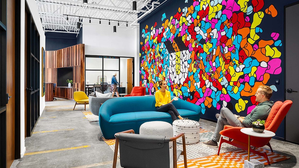 A couple of people sitting on a couch in a room with a wall of art.