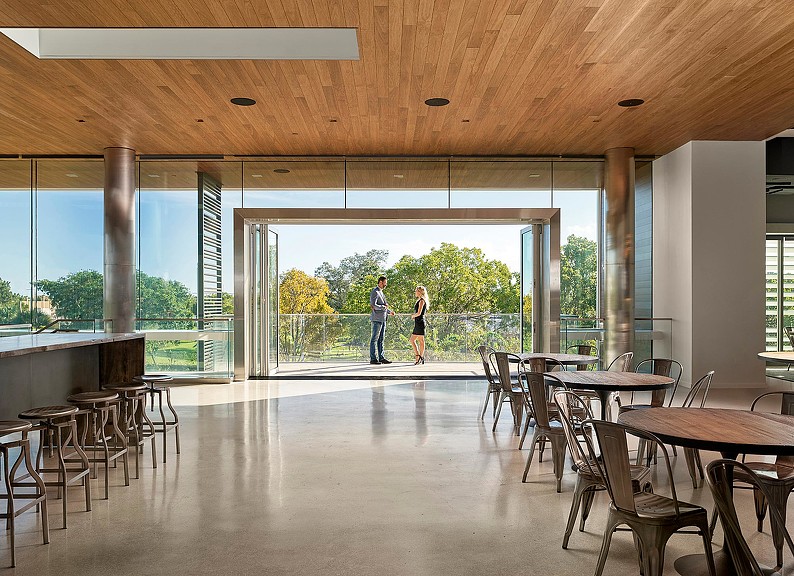 A couple of people walking in a large room with tables and chairs.