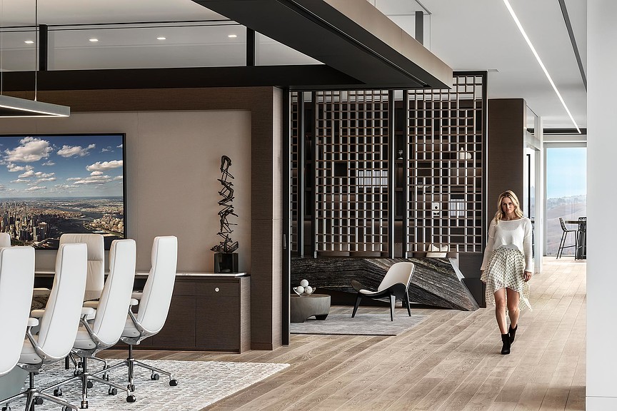 A person walking in a room with chairs and a large window.