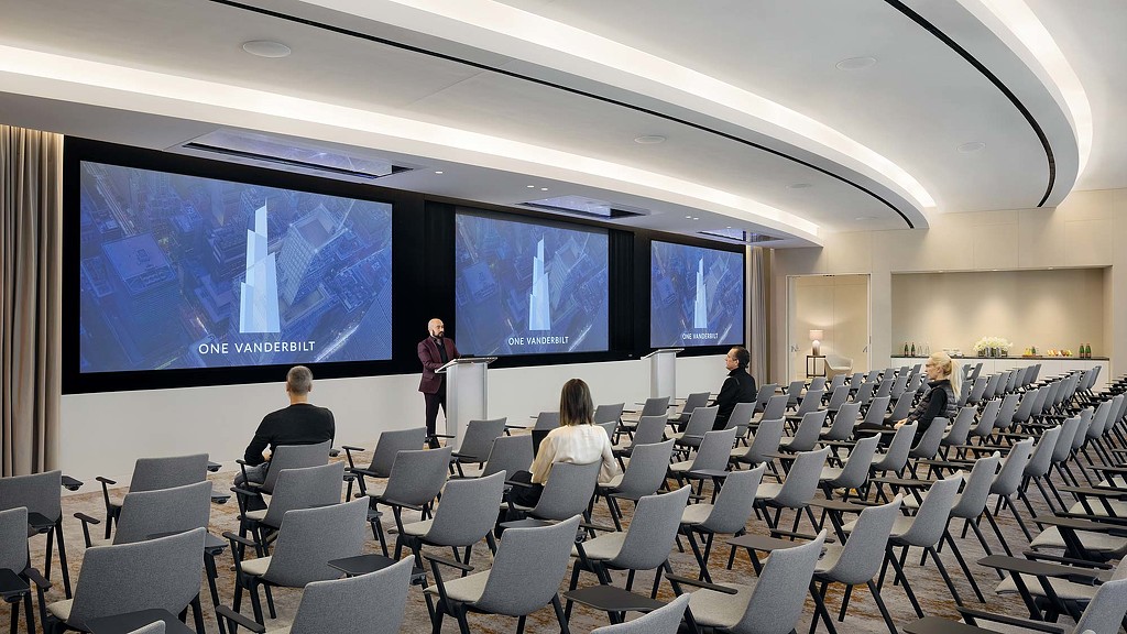 A group of people sitting in chairs in front of a large screen.