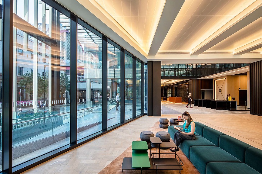 A person sitting on a couch in a large room with large windows.