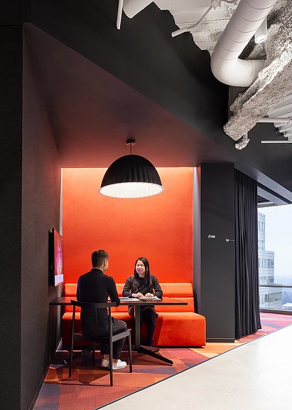 A man and a woman sitting at a table in a room with a large orange wall and a.