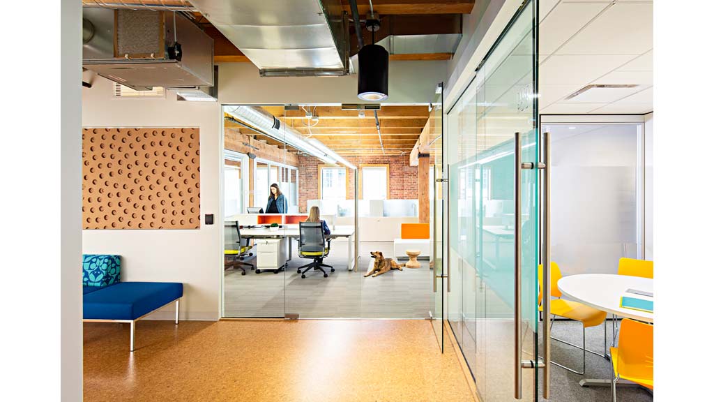 A room with a table chairs and a person sitting at a desk.