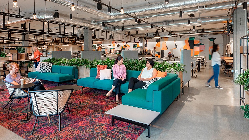 People sitting on couches in a room with people walking around.