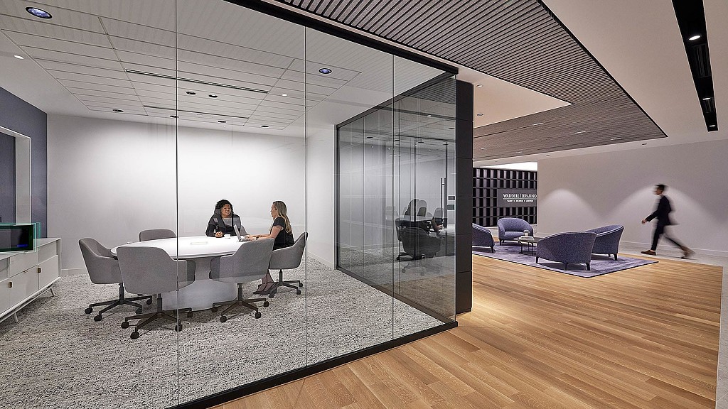 A room with a glass wall and a table with chairs and a person walking by.