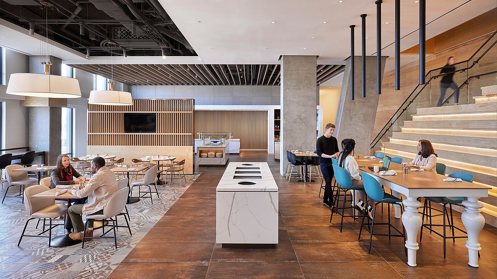 People sitting at tables in a large room with a staircase.